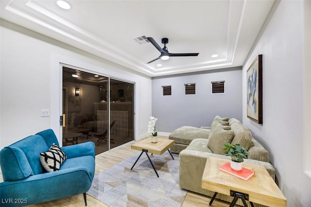 living room with light hardwood / wood-style floors, a tray ceiling, and ceiling fan