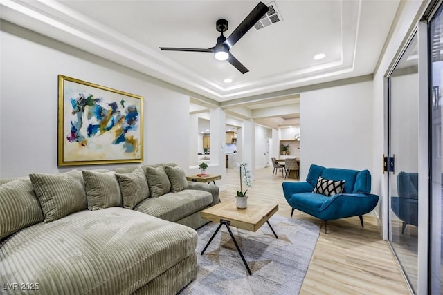 living room featuring light wood-type flooring, ceiling fan, and a raised ceiling