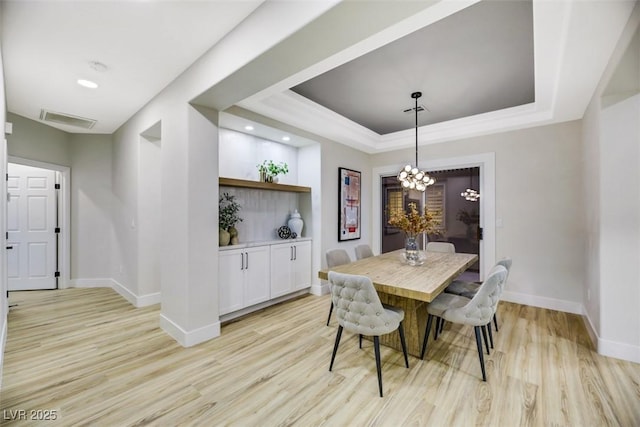 dining space with an inviting chandelier, light hardwood / wood-style flooring, and a raised ceiling