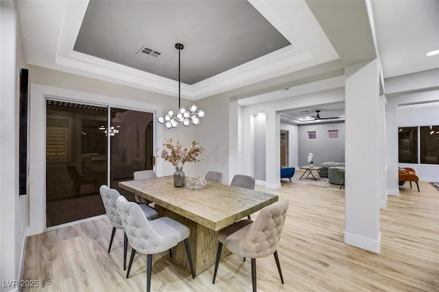 dining area featuring ceiling fan with notable chandelier, a tray ceiling, and light wood-type flooring