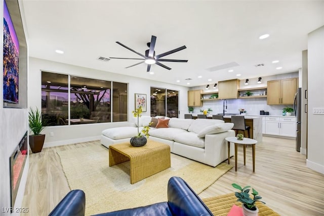 living room with ceiling fan, sink, and light wood-type flooring