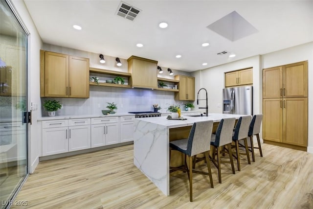 kitchen with light hardwood / wood-style flooring, decorative backsplash, a kitchen island with sink, and stainless steel refrigerator with ice dispenser