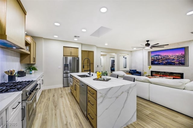 kitchen featuring appliances with stainless steel finishes, sink, light hardwood / wood-style flooring, an island with sink, and light stone counters