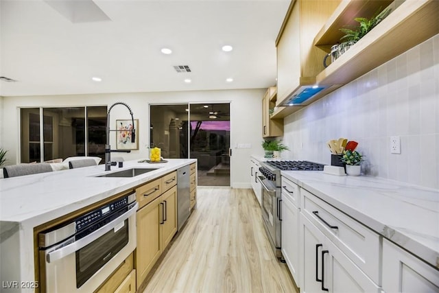 kitchen featuring light stone countertops, stainless steel appliances, decorative backsplash, sink, and light wood-type flooring