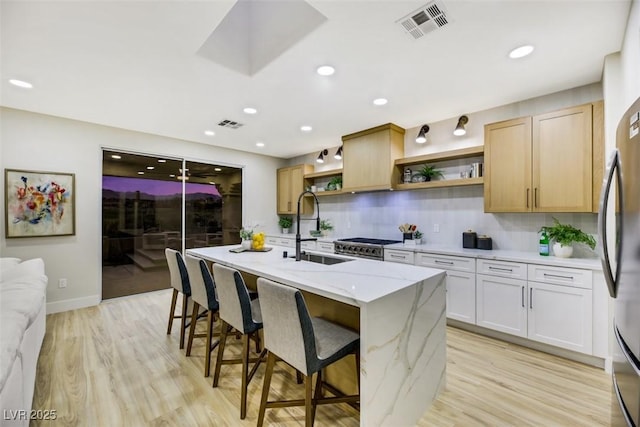 kitchen featuring white cabinetry, sink, light hardwood / wood-style flooring, an island with sink, and light stone counters