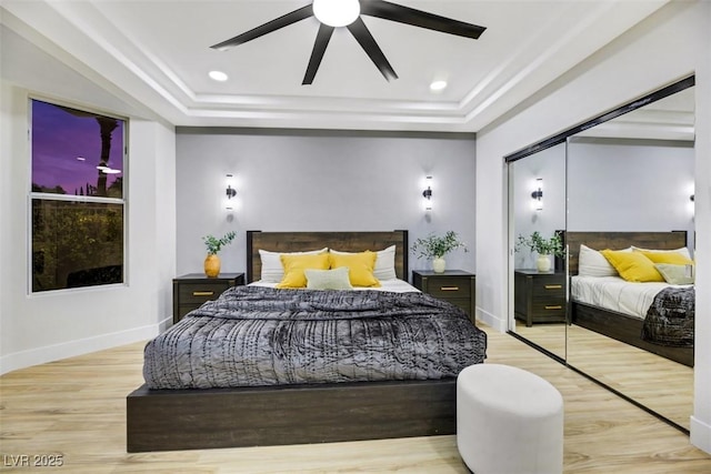 bedroom with a closet, ceiling fan, light wood-type flooring, and a tray ceiling