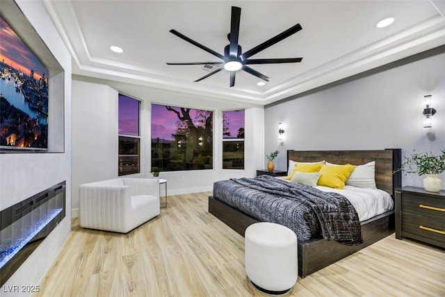 bedroom featuring ceiling fan, light hardwood / wood-style floors, and a tray ceiling