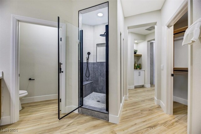 bathroom with wood-type flooring, toilet, and a shower with door