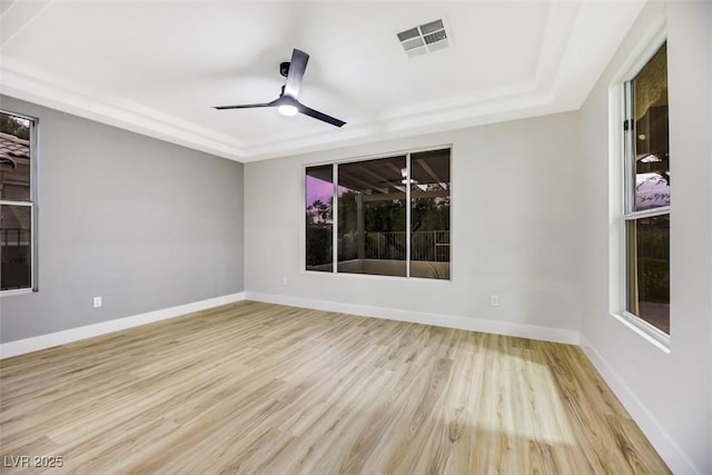 unfurnished room featuring ceiling fan, a tray ceiling, and light wood-type flooring