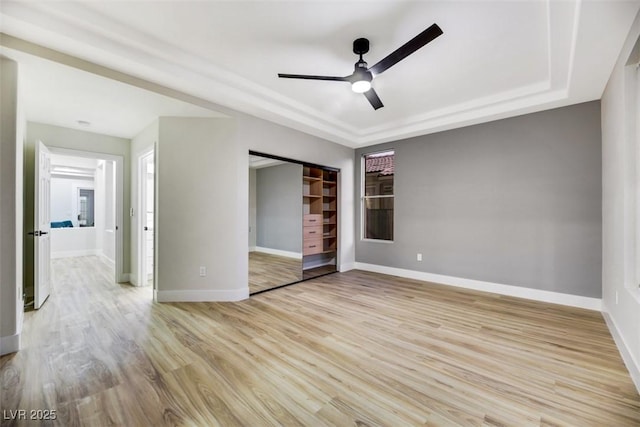 unfurnished bedroom with ceiling fan, light hardwood / wood-style floors, a tray ceiling, and a closet