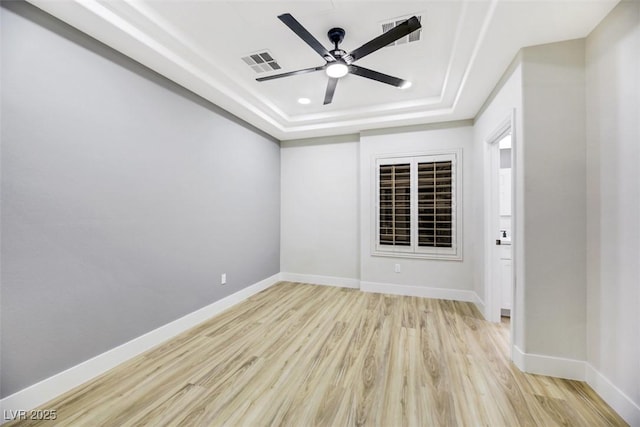 empty room featuring ceiling fan, light hardwood / wood-style flooring, and a tray ceiling