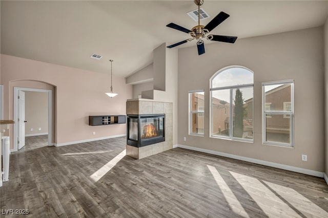 unfurnished living room featuring a tiled fireplace, wood-type flooring, high vaulted ceiling, and ceiling fan