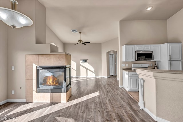 kitchen with a tile fireplace, ceiling fan, high vaulted ceiling, white cabinets, and light wood-type flooring