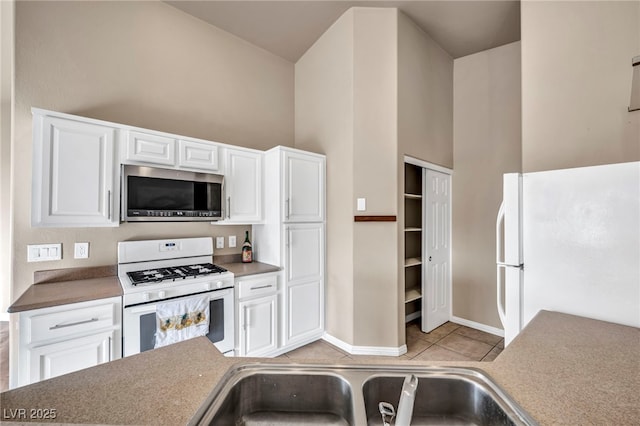 kitchen with light tile patterned floors, white appliances, sink, a towering ceiling, and white cabinets