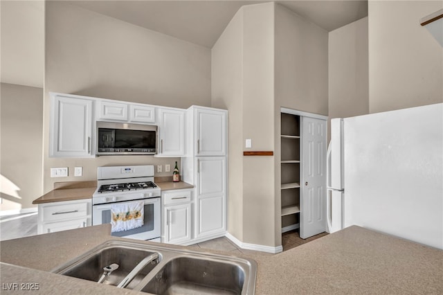 kitchen featuring sink, white appliances, light tile patterned floors, a high ceiling, and white cabinets