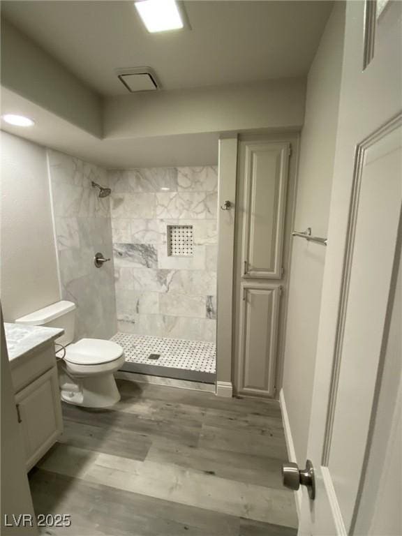 bathroom with vanity, toilet, tiled shower, and wood-type flooring