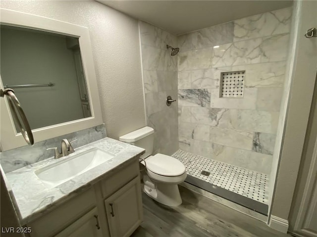 bathroom with hardwood / wood-style floors, toilet, vanity, and a tile shower