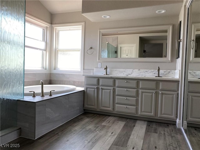 bathroom with tiled bath, hardwood / wood-style floors, vanity, and vaulted ceiling