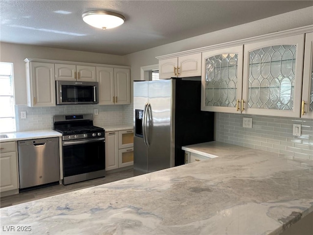 kitchen with backsplash, white cabinetry, light stone countertops, and stainless steel appliances