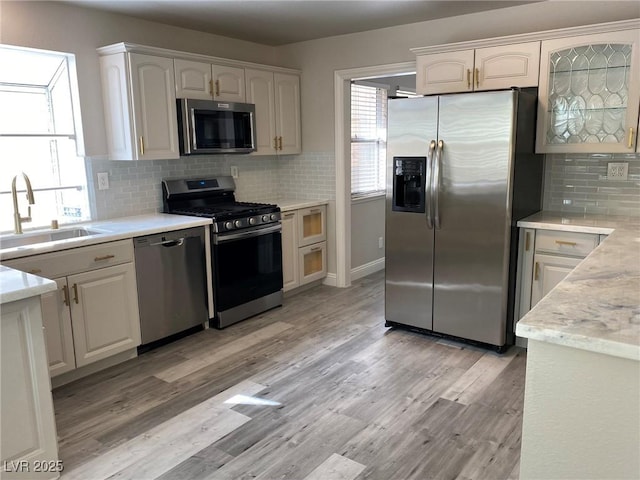 kitchen with light hardwood / wood-style flooring, sink, white cabinets, tasteful backsplash, and stainless steel appliances