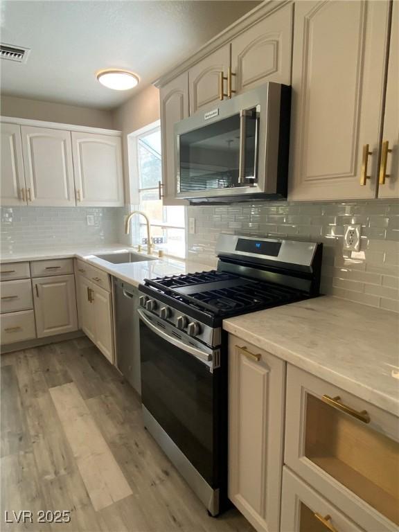 kitchen with sink, light wood-type flooring, tasteful backsplash, and appliances with stainless steel finishes