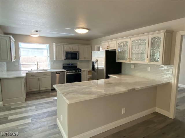 kitchen featuring kitchen peninsula, appliances with stainless steel finishes, sink, white cabinetry, and decorative backsplash