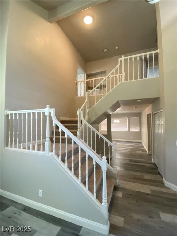 staircase with a towering ceiling, beam ceiling, and hardwood / wood-style floors