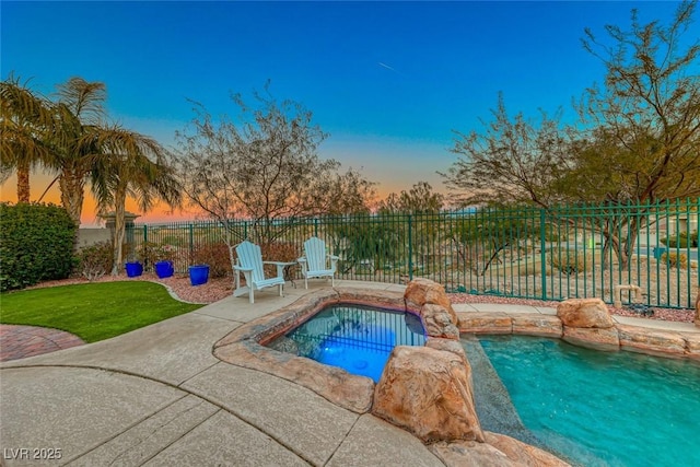 pool at dusk with an in ground hot tub and a patio