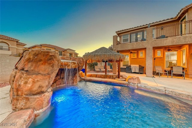 pool at dusk featuring a patio area, ceiling fan, a gazebo, and pool water feature