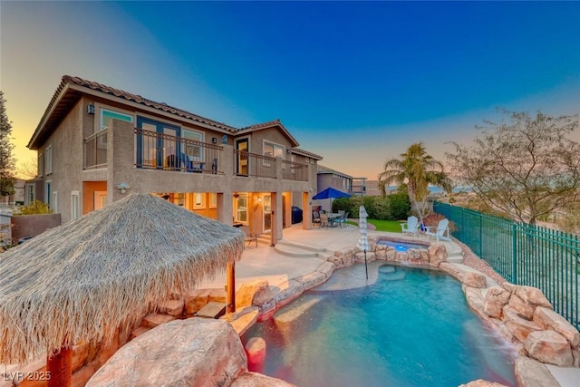 pool at dusk with pool water feature, an in ground hot tub, and a patio area