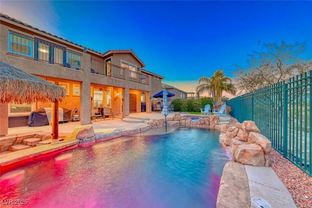 pool at dusk featuring pool water feature and a patio