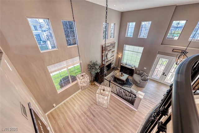 living room with a wealth of natural light, hardwood / wood-style floors, a stone fireplace, and a towering ceiling