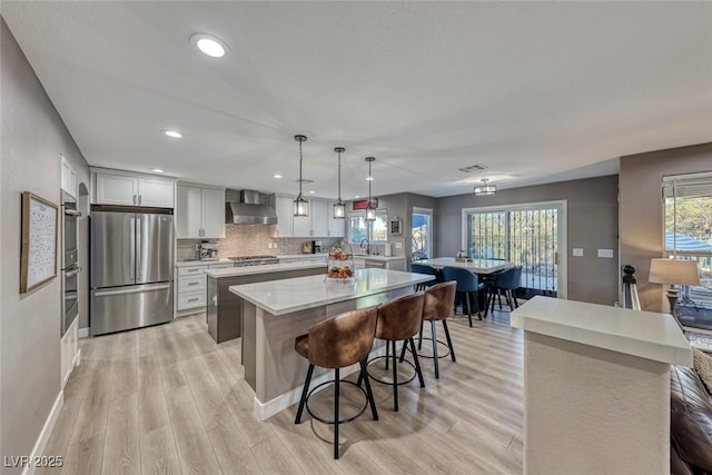 kitchen with pendant lighting, tasteful backsplash, a center island, wall chimney range hood, and stainless steel appliances