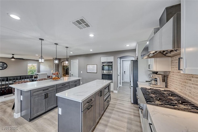 kitchen with a center island, hanging light fixtures, wall chimney range hood, stainless steel appliances, and gray cabinets