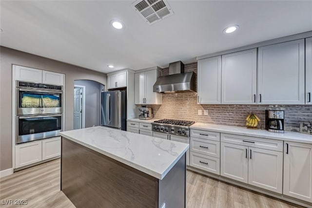 kitchen featuring light stone countertops, white cabinets, backsplash, stainless steel appliances, and wall chimney exhaust hood