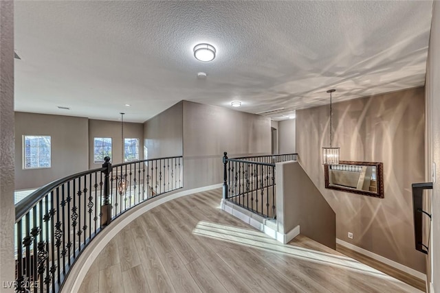 hall featuring a notable chandelier, light hardwood / wood-style flooring, and a textured ceiling