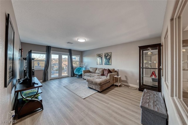 living room featuring light hardwood / wood-style floors, a textured ceiling, and french doors