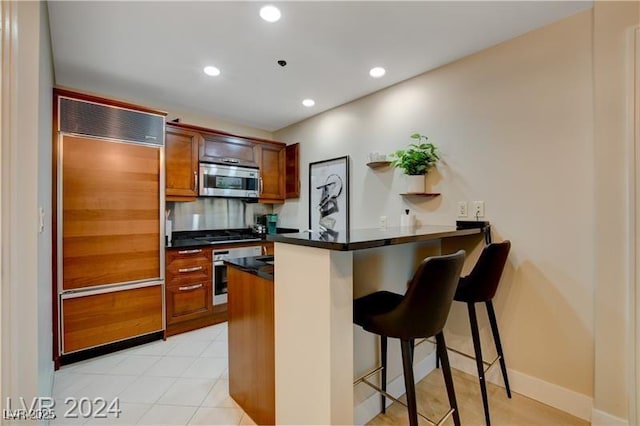 kitchen with decorative backsplash, a breakfast bar, appliances with stainless steel finishes, and kitchen peninsula