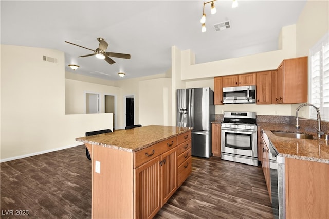 kitchen with appliances with stainless steel finishes, sink, dark wood-type flooring, light stone countertops, and a kitchen island