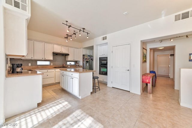 kitchen featuring white cabinets, backsplash, a kitchen breakfast bar, a center island, and black appliances