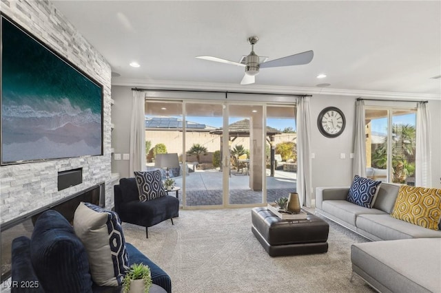 carpeted living room with crown molding, ceiling fan, and a stone fireplace