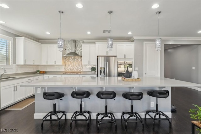 kitchen featuring wall chimney exhaust hood, pendant lighting, a spacious island, and appliances with stainless steel finishes