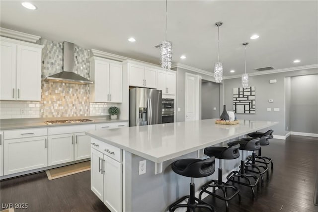 kitchen with a large island, white cabinets, appliances with stainless steel finishes, and wall chimney exhaust hood