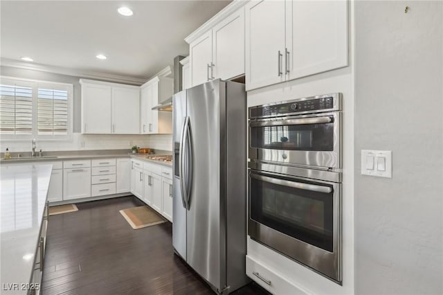 kitchen with appliances with stainless steel finishes, wall chimney range hood, white cabinetry, dark hardwood / wood-style flooring, and sink