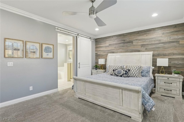 carpeted bedroom featuring ceiling fan, ensuite bathroom, a barn door, ornamental molding, and wooden walls