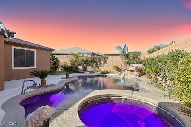 pool at dusk featuring an in ground hot tub and a patio area