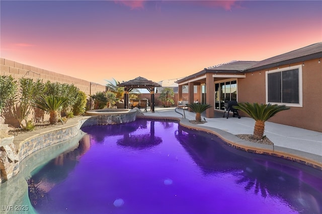 pool at dusk featuring an in ground hot tub, a patio area, and a gazebo