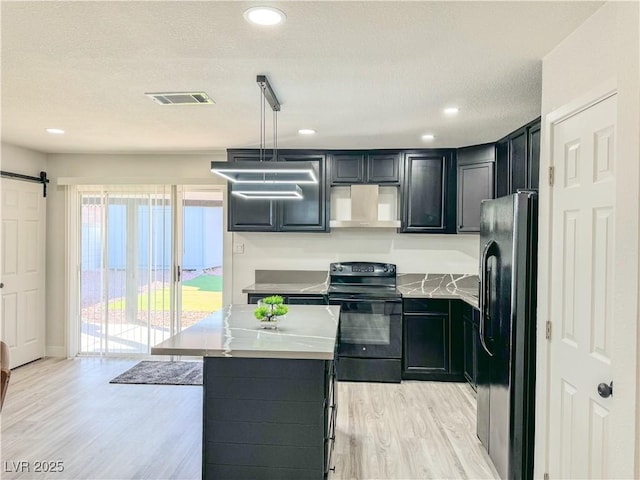 kitchen featuring black appliances, wall chimney exhaust hood, light hardwood / wood-style floors, hanging light fixtures, and a barn door