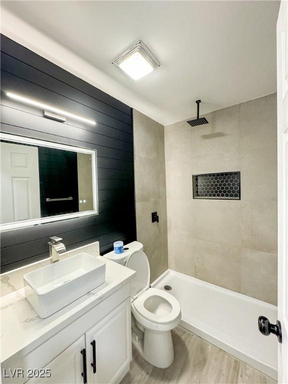 bathroom featuring hardwood / wood-style floors, tiled shower, toilet, and vanity