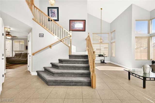 stairs with ceiling fan with notable chandelier, tile patterned flooring, and high vaulted ceiling